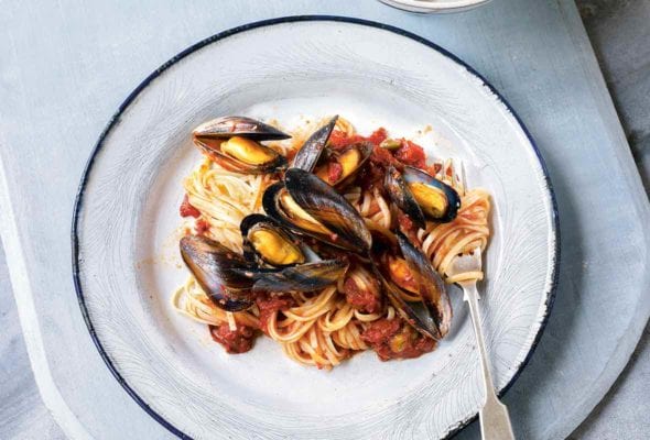 A white plate topped with linguine and mussels in a red dress