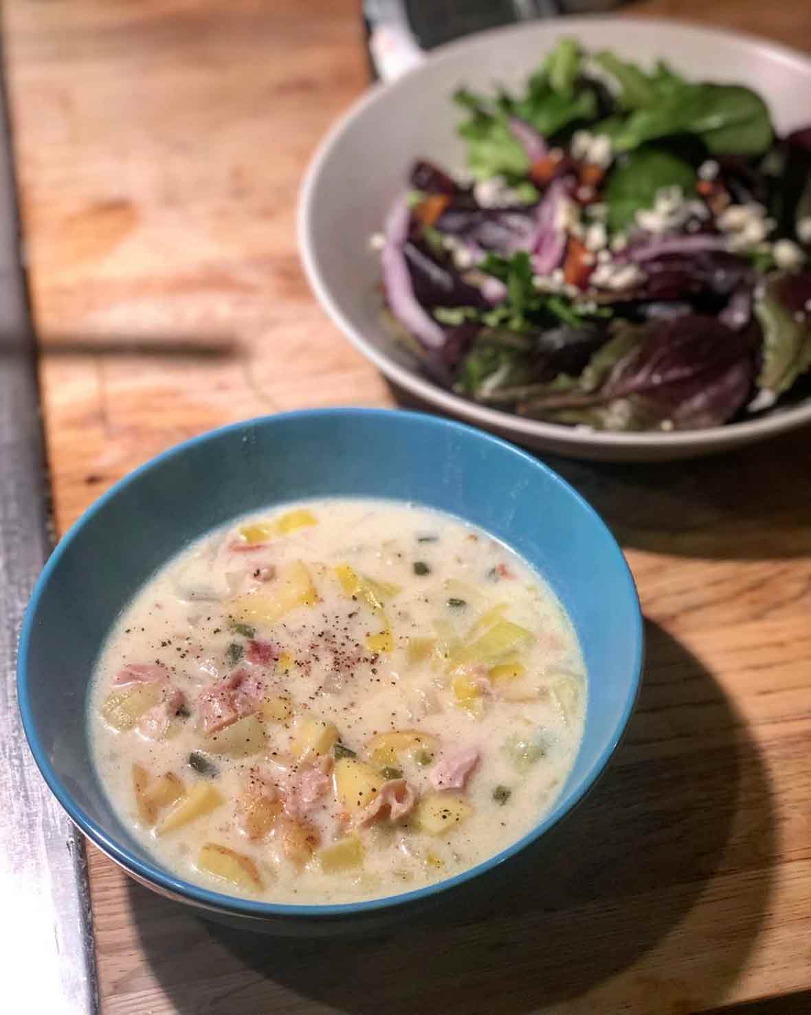 A bowl of creamy New England clam chowder with a side salad
