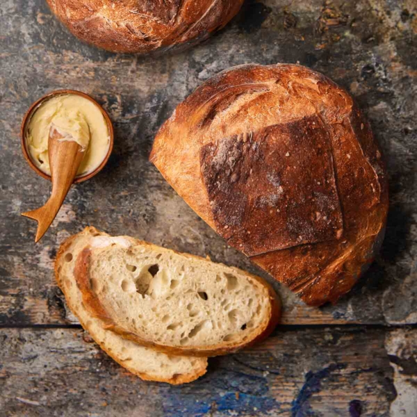 Two loaves of no-knead artisan bread, one with two slices cut from it and a dish of butter nearby.