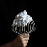 A hand holding a stand-mixer whisk covered in vegan meringue
