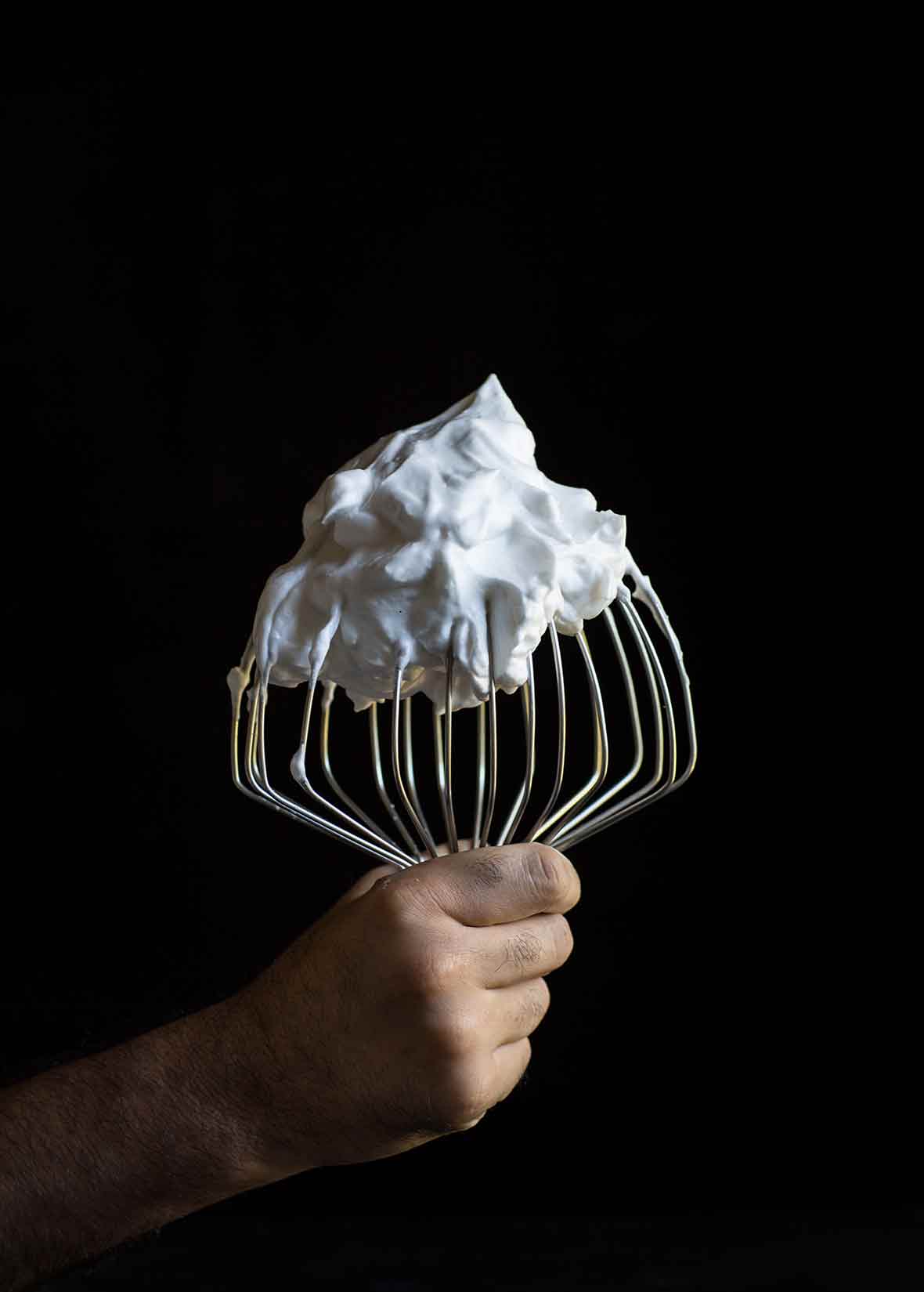 A hand holding a stand-mixer whisk covered in vegan meringue
