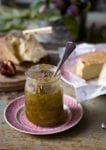 A jar of celery marmalade with a spoon in it and several types of cheese in the background