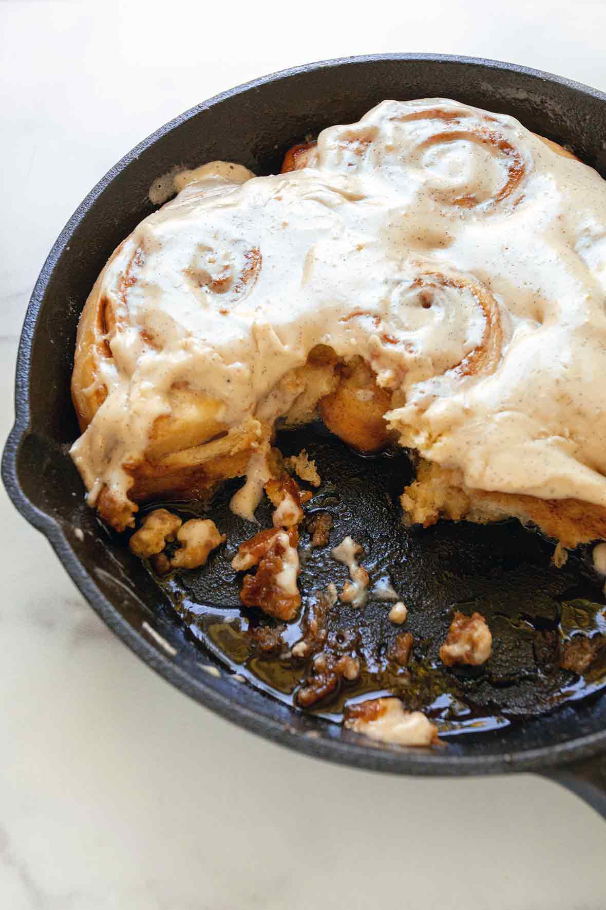 A cast-iron skillet half filled with skillet cinnamon rolls, the other half eaten.