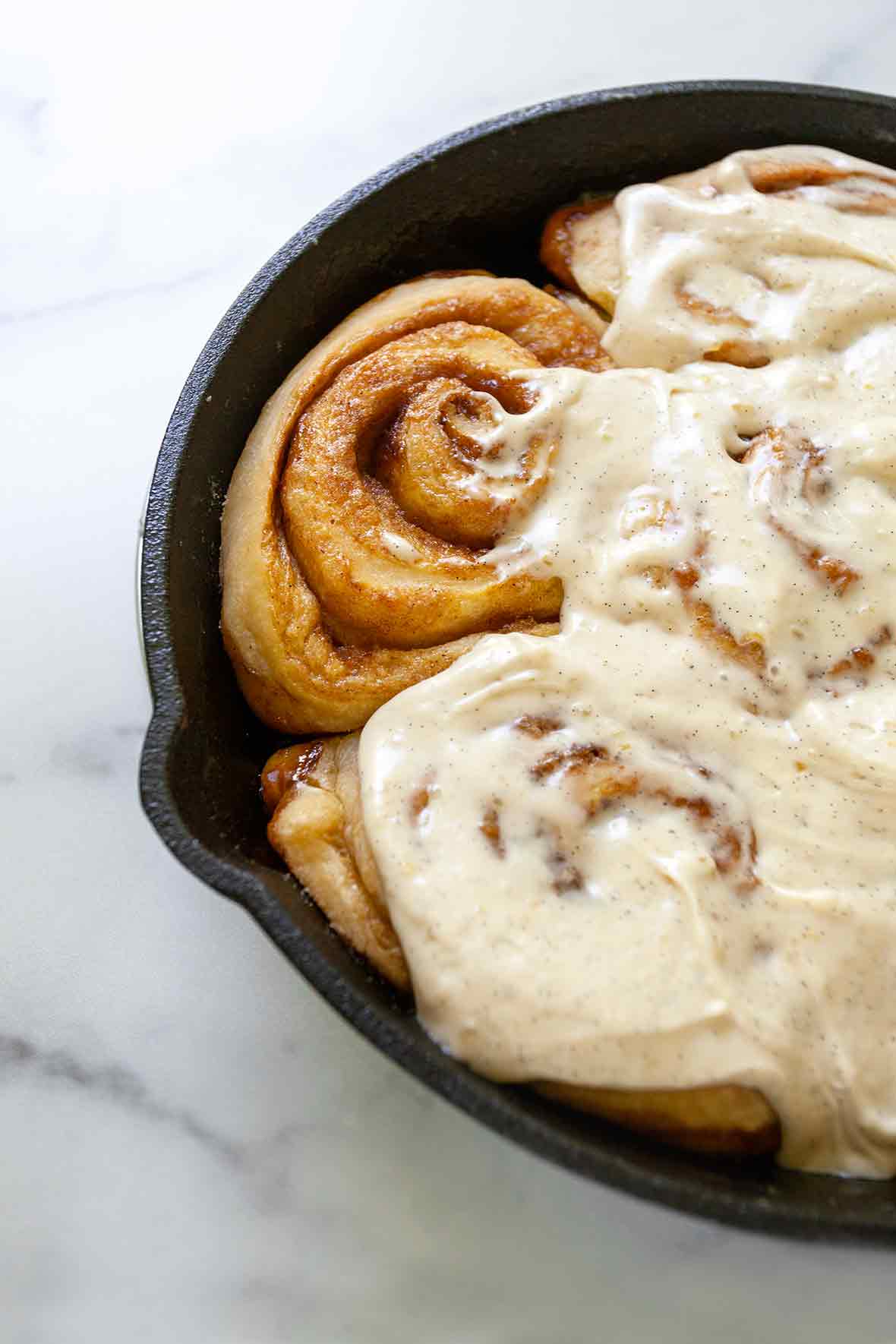 A cast iron skillet filled with half frosted skillet cinnamon rolls