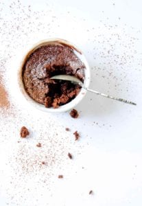 A white ramekin filled with a partially eaten double chocolate souffle and a spoon resting inside
