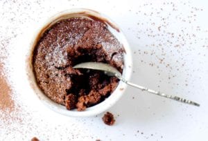 A white ramekin filled with a partially eaten double chocolate souffle and a spoon resting inside
