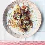 A white plate with striped edges filled with potatoes and lamb meatballs with tahini