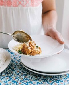 A woman spooning a portion of slow cooker Indian butter chicken and rice into a white bowl
