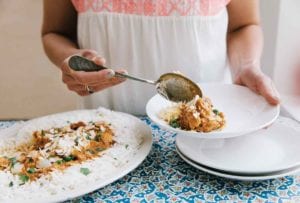A woman spooning a portion of slow cooker Indian butter chicken and rice into a white bowl