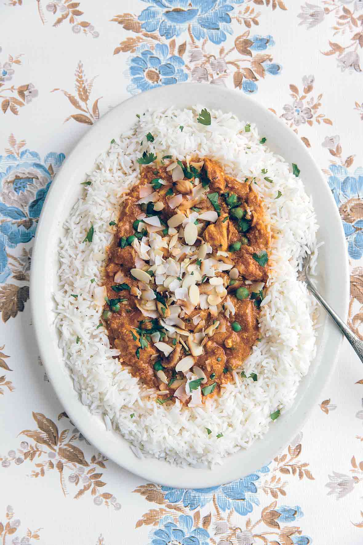 A white serving platter filled with slow cooker Indian butter chicken on a bed of basmati rice, topped with almonds and coconut
