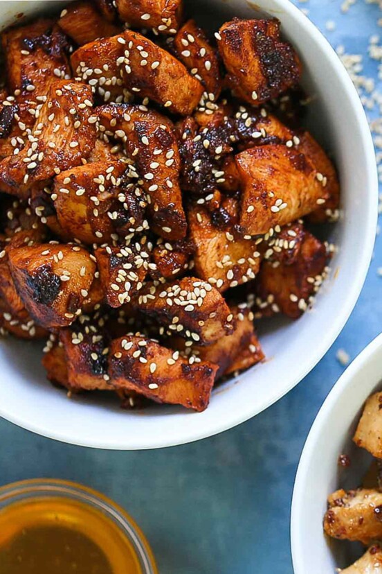 A white bowl filled with spicy Korean chicken and sprinkled with sesame seeds.