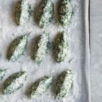 A rimmed baking sheet with 9 uncooked spinach and ricotta gnudi