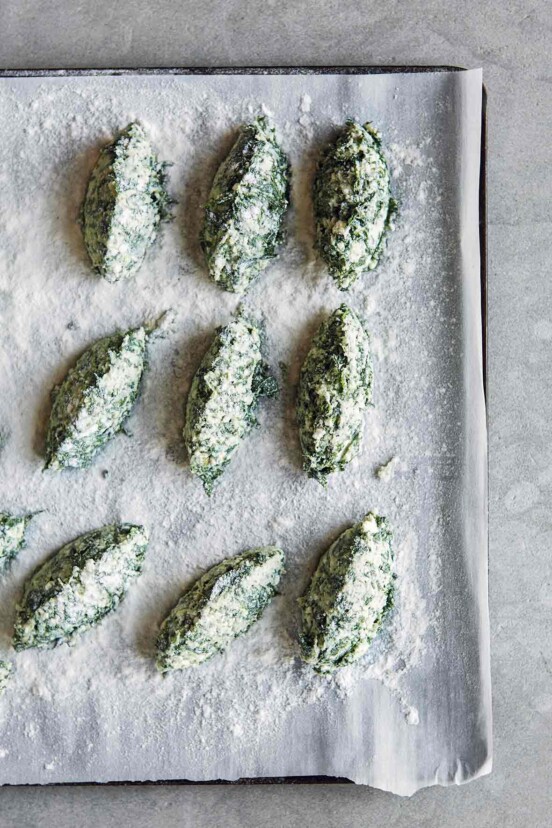 A rimmed baking sheet with 9 uncooked spinach and ricotta gnudi