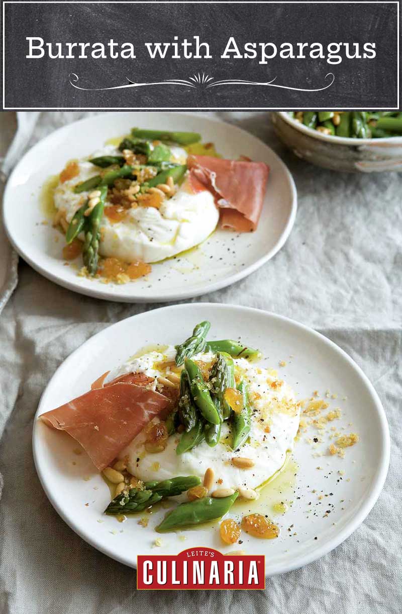 Two plates with burrata topped with asparagus, pine nuts, raisins, and prosciutto.