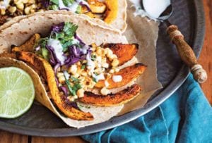 A platter of butternut squash tacos made with tortillas filled with strips of roasted squash, corn, cabbage, guacamole, and sour cream.