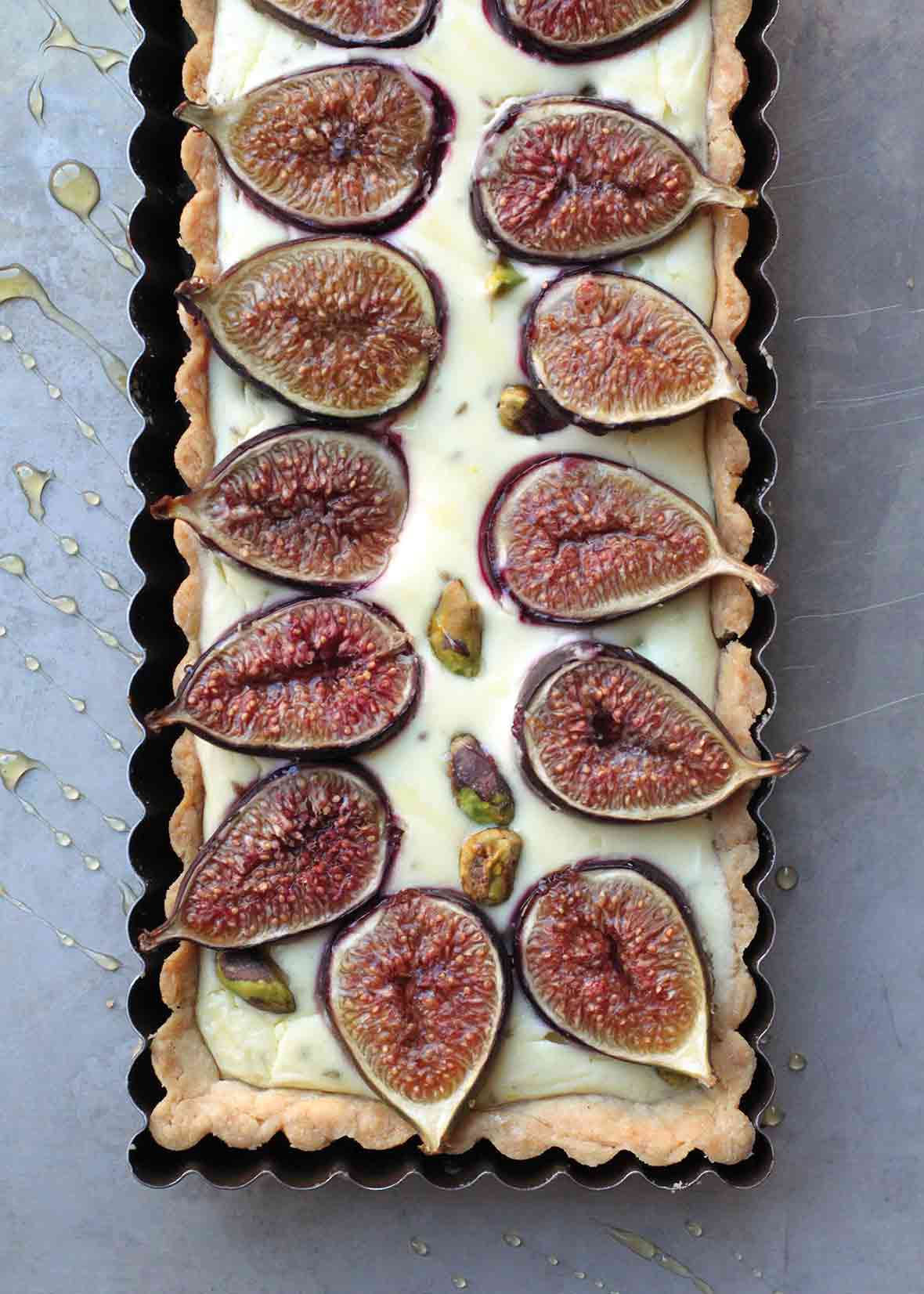 A cooked rectangular fig tart with goat cheese and pistachios in a tart pan