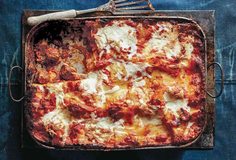Meatball lasagna, with one piece missing, in a large baking dish beside a spatula.