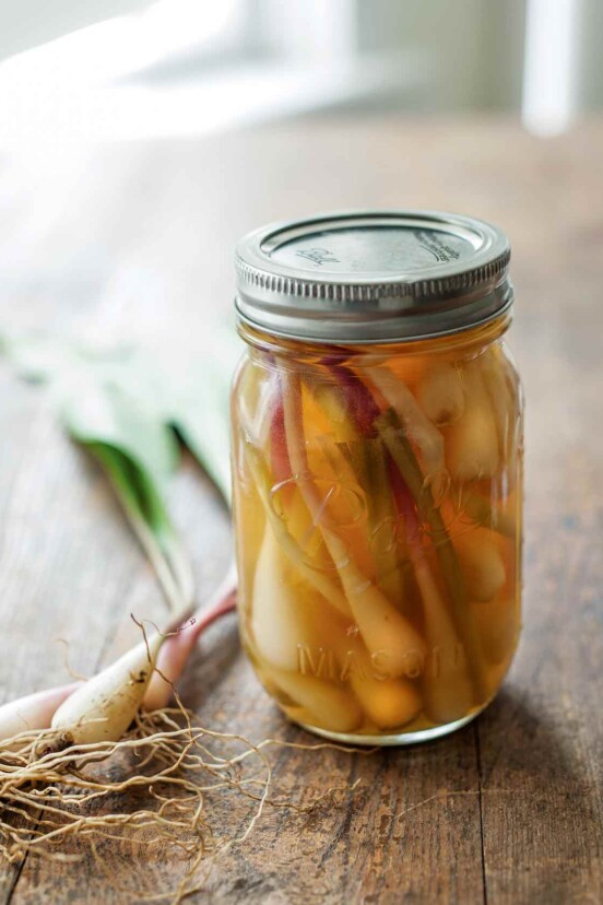 A canning jar filled with quick pickled ramps and some fresh ramps lying beside the jar.