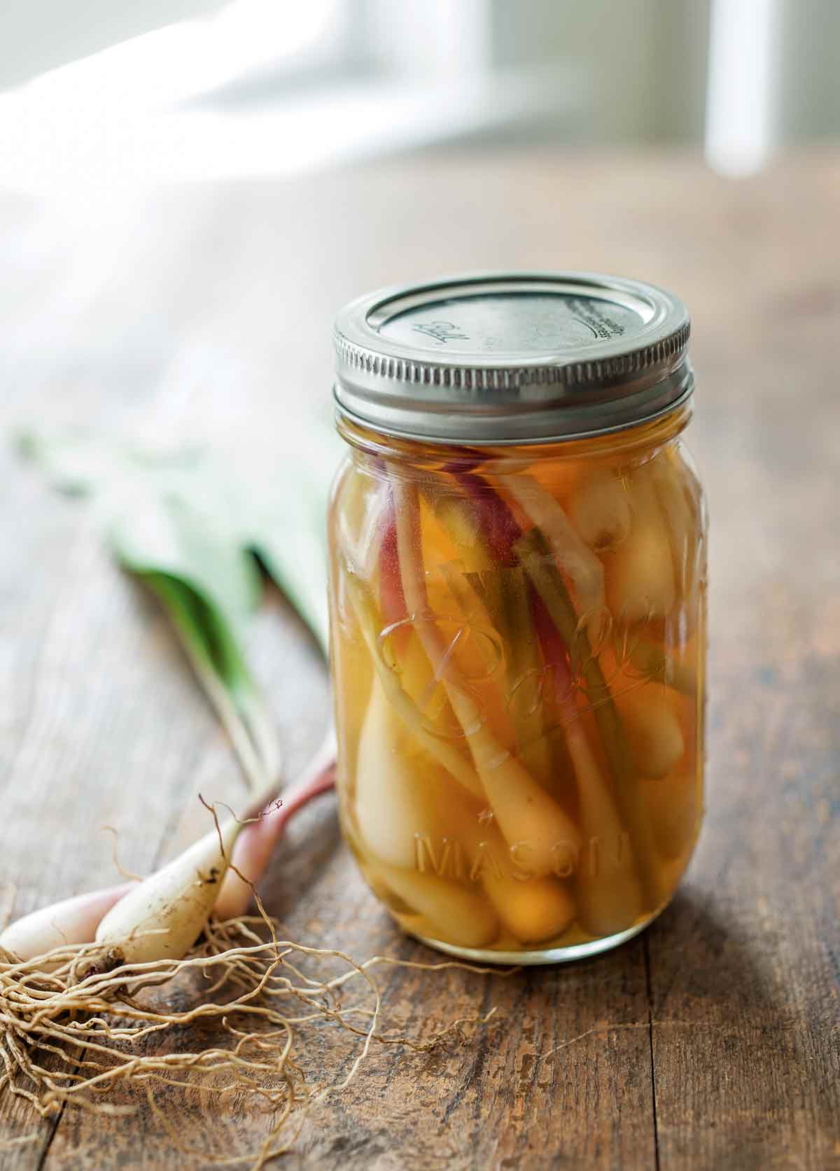 A canning jar filled with quick pickled ramps and some fresh ramps lying beside the jar.