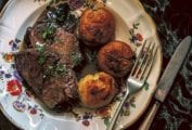 A china plate with three slices of beef braised in red wine and sprinkled with parsley, and three roasted potatoes