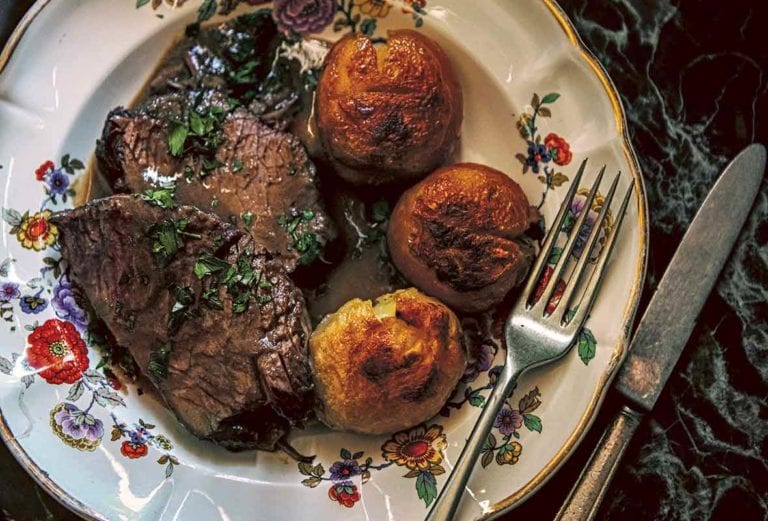 A china plate with three slices of beef braised in red wine and sprinkled with parsley, and three roasted potatoes