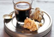 Two pieces of almond biscotti on a stack of plates with a glass of coffee