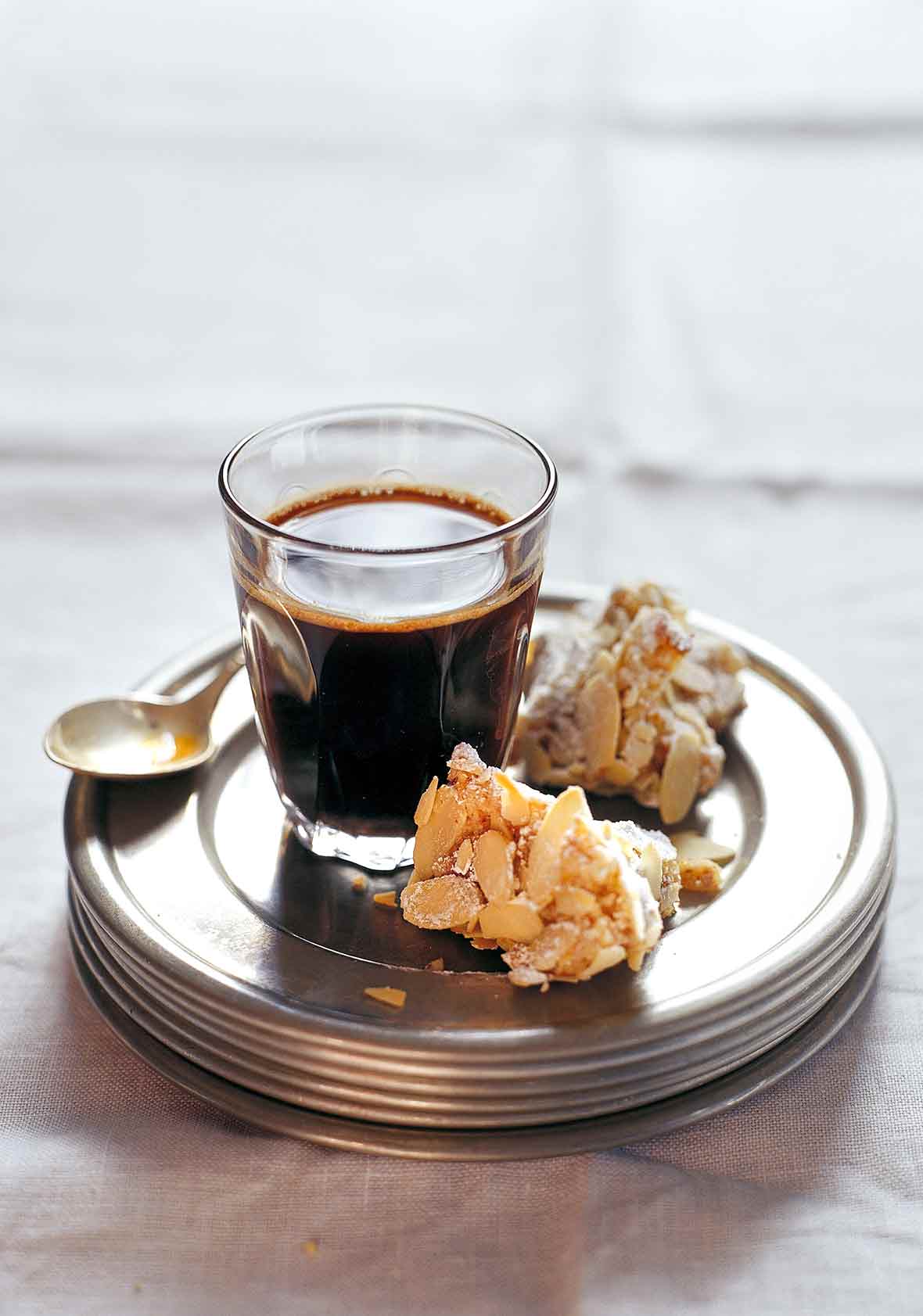 Two pieces of almond biscotti on a stack of plates with a glass of coffee