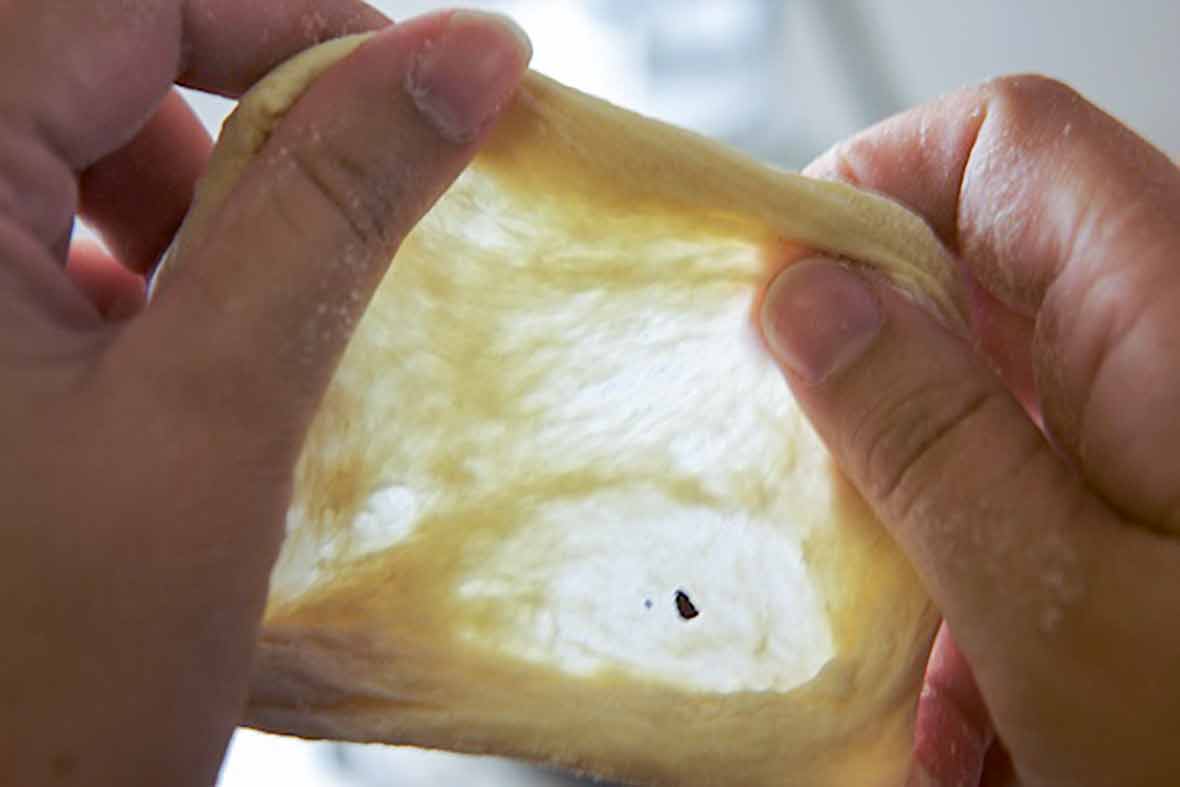 A person stretching a piece of bread dough.