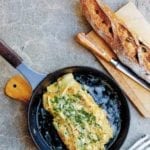A black skillet containing a cheese omelet, topped with chives and Gruyere