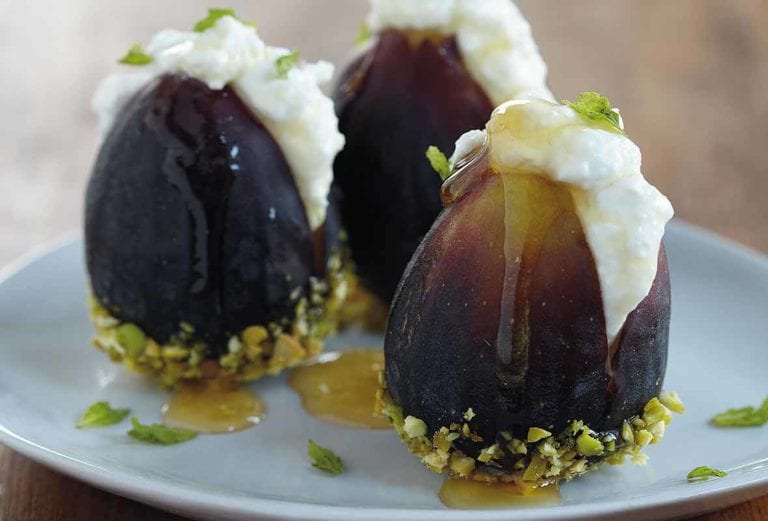 Three fresh figs with ricotta and honey and dipped in pistachios on a white plate