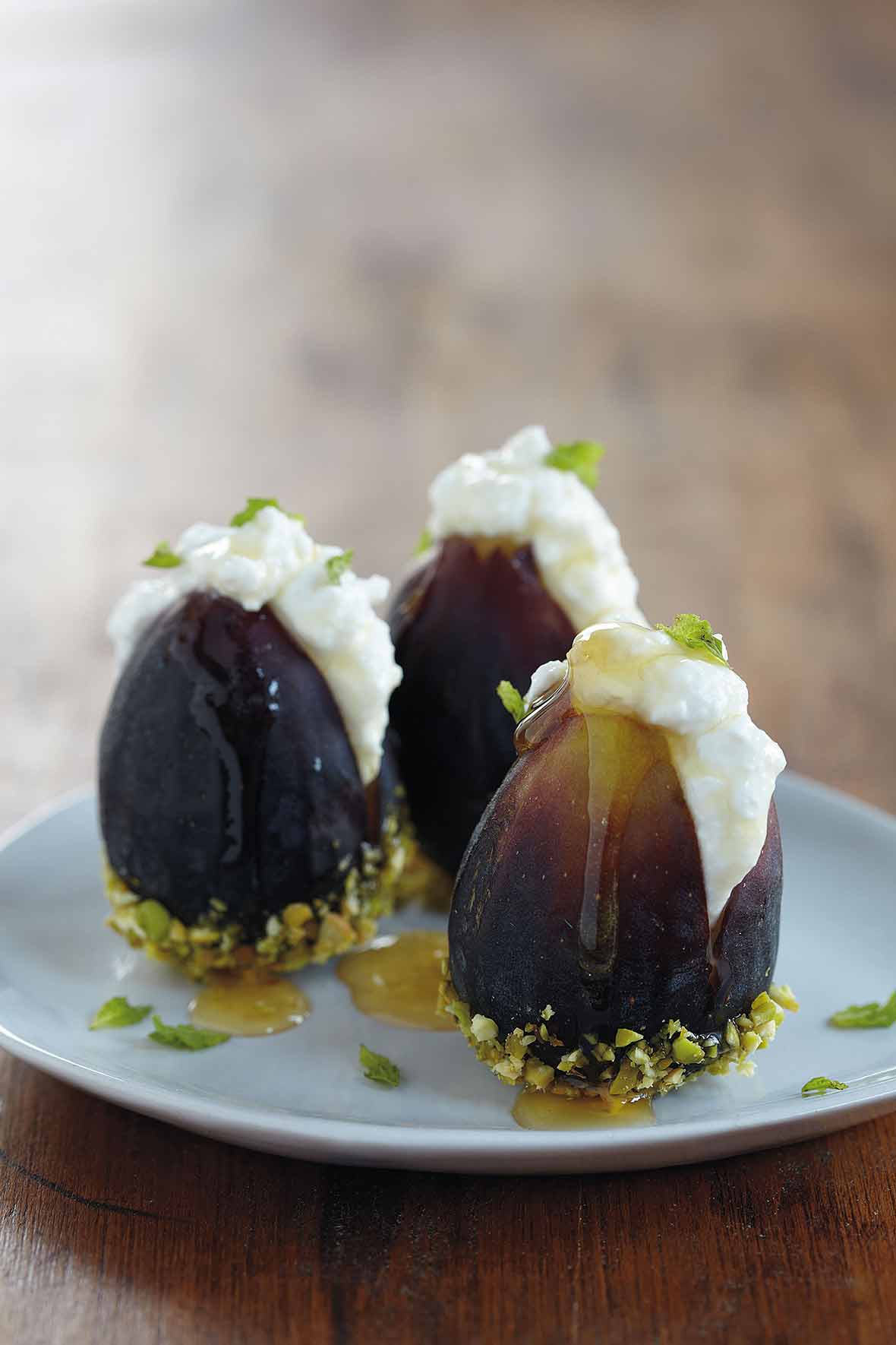 Three fresh figs with ricotta and honey and dipped in pistachios on a white plate