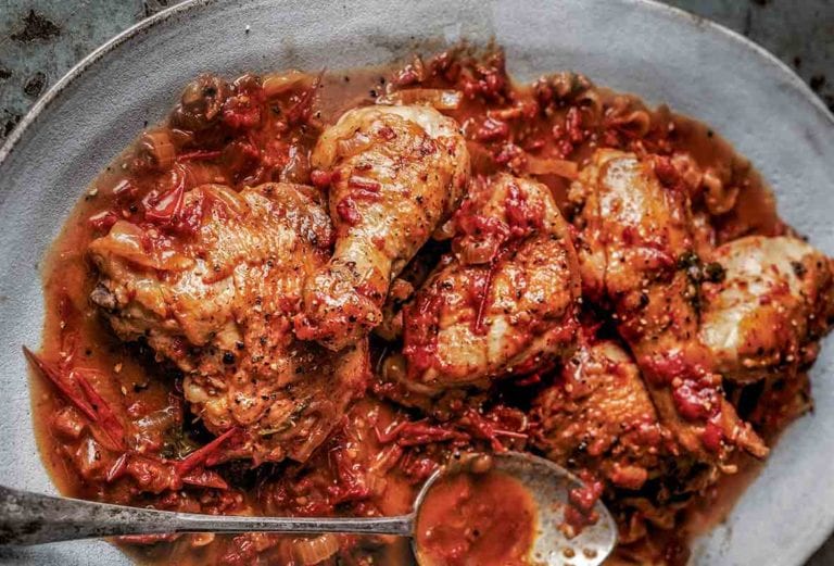 A grey platter of Italian-style chicken braised in wine with a spoon resting on top