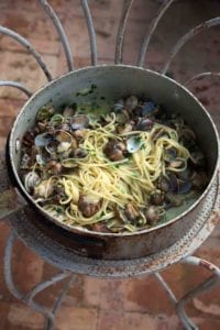 A large metal pot filled with linguine with clams resting on a metal stand