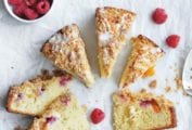Nine slices of raspberry peach coffee cake with a bowl of raspberries nearby and some more raspberries scattered around the cake.