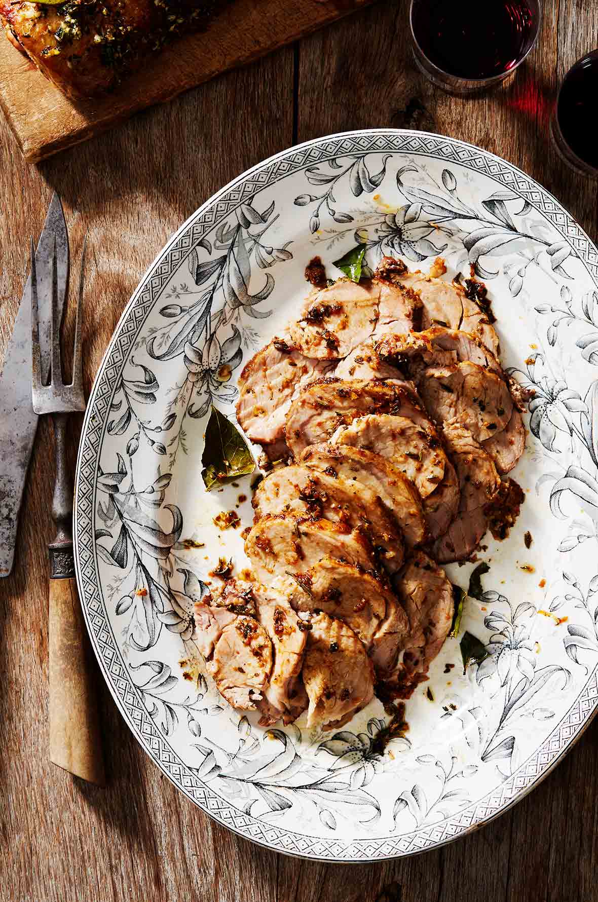 A black and white decorative platter filled with Tuscan roast pork and scattered with bay leaves