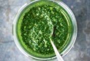 A glass jar filled with green sauce with a spoon resting inside.