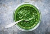 A glass jar filled with green sauce with a spoon resting inside.