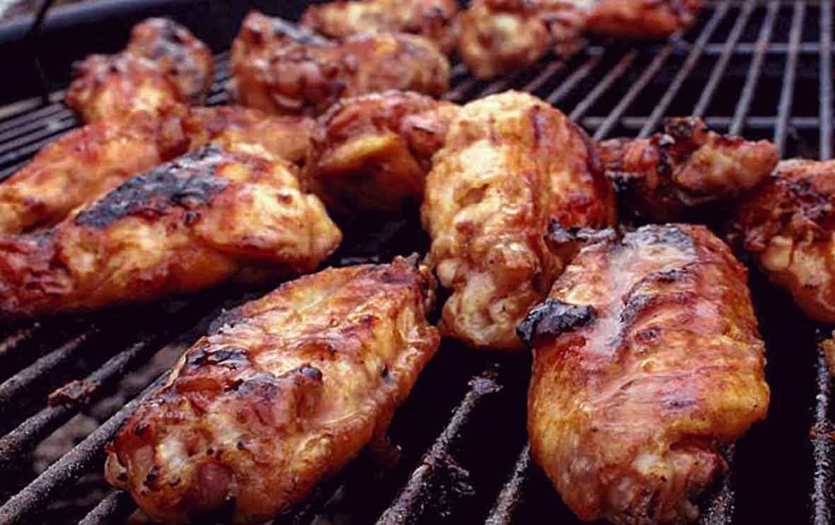 Grilled chicken wings with maple bourbon sauce on a grill grate.