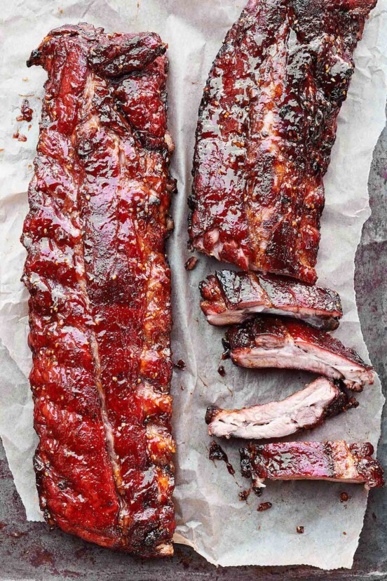 Two slabs of honey teriyaki ribs, one partially cut into ribs on a sheet of parchment.