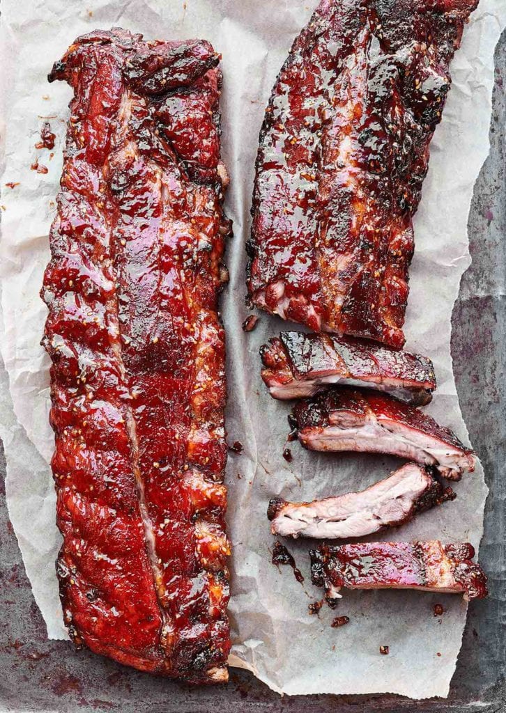 Two slabs of honey teriyaki ribs, one partially cut into ribs on a sheet of parchment.