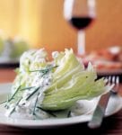 A white plate topped with an iceberg wedge with blue cheese dressing.