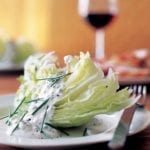 A white plate topped with an iceberg wedge with blue cheese dressing.