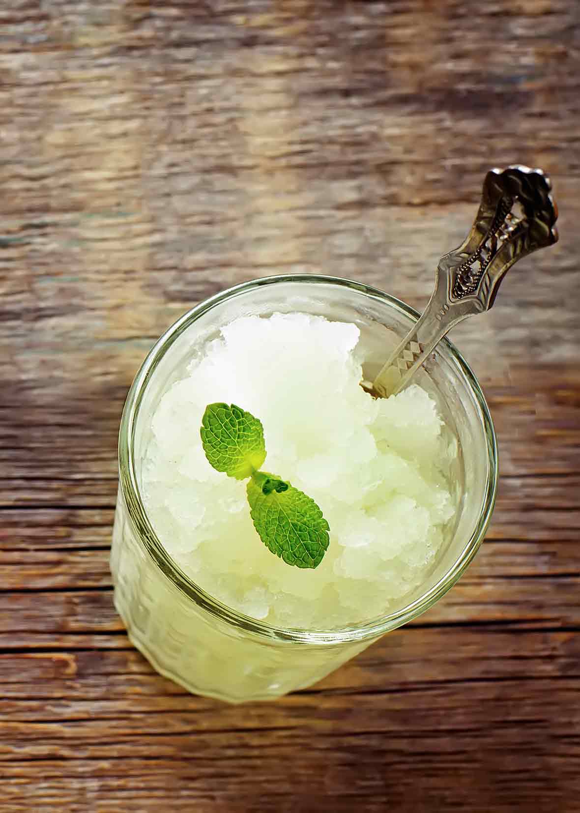 A glass filled with margarita granita, topped with a lime sprig and a spoon resting in the glass.