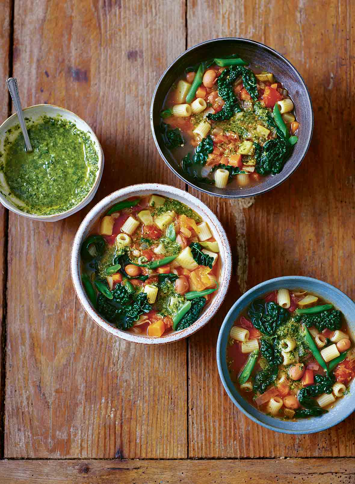 Three bowls of minestrone soup and a small bowl of pesto.