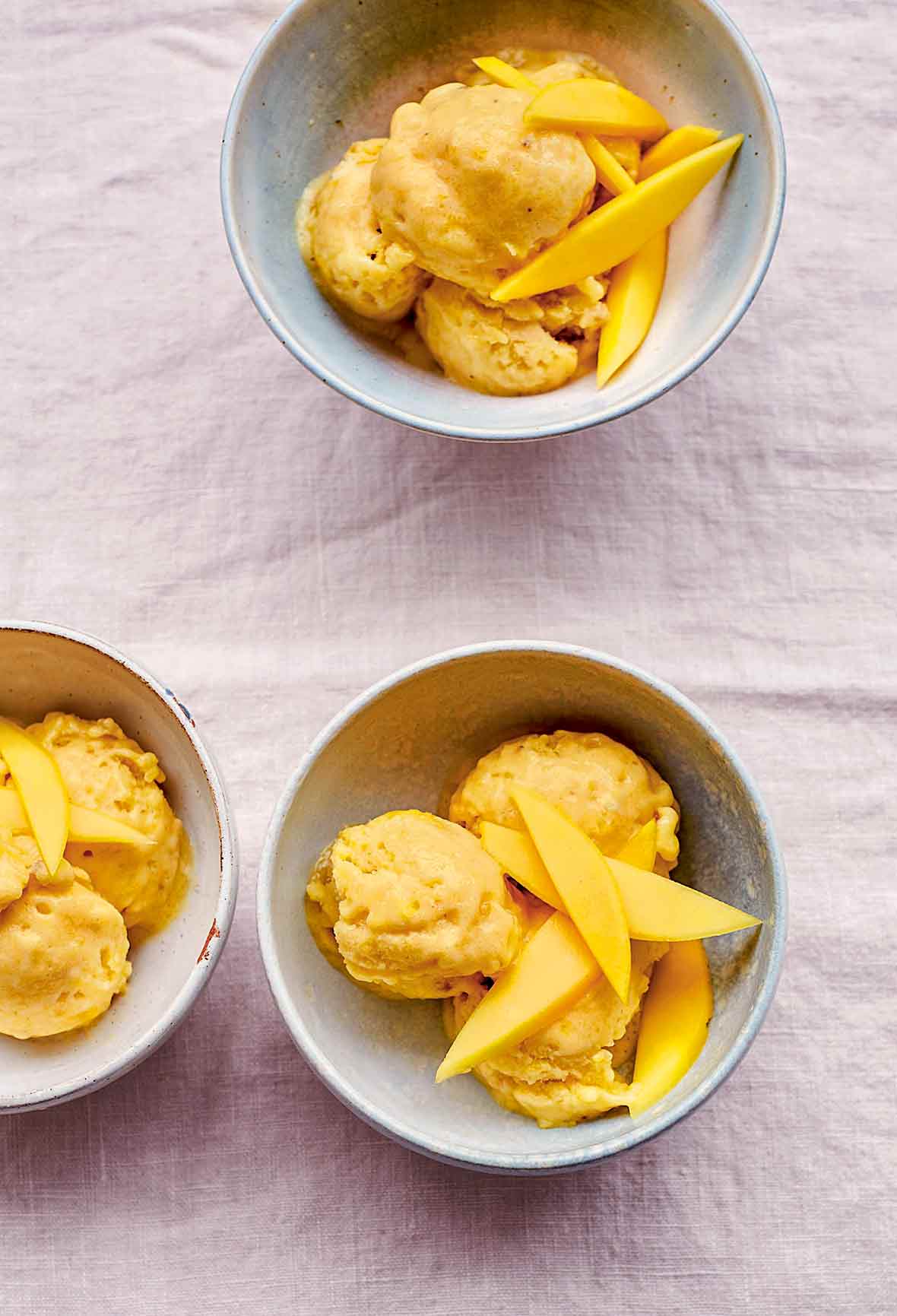 Three bowls of vegan mango ice cream topped with mango slices.