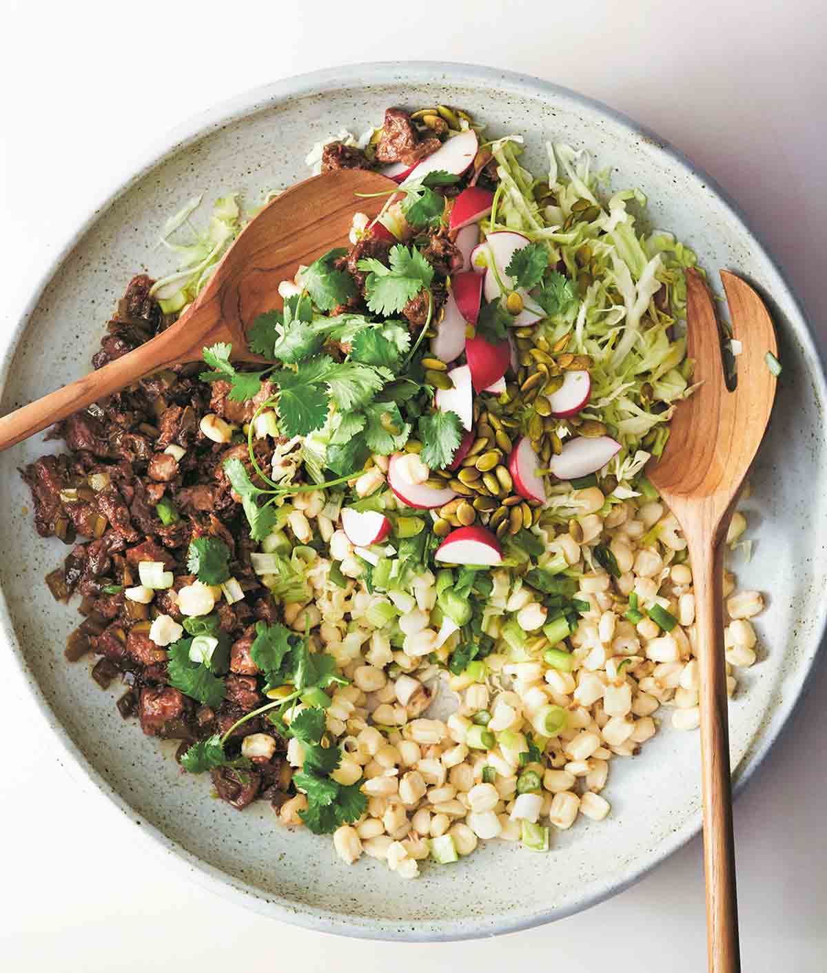 A ceramic bowl filled with posole salad, including hominy, crispy pork, cabbage, radish, pepitas, and cilantro.