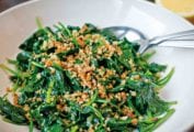 A white serving bowl filled with sauteed spinach and bread crumbs.