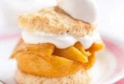 A spiced peach shortcake on a white plate with spiced peaches layered between two biscuit halves and topped with whipped cream.