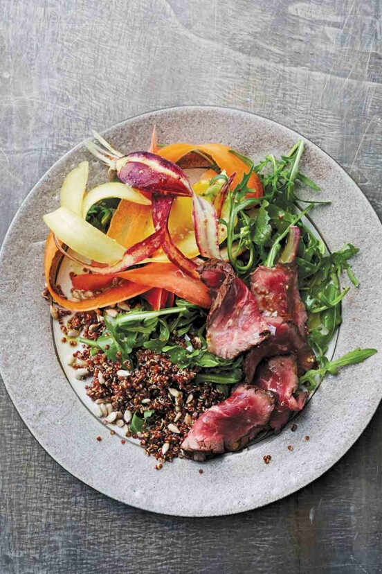 A grey plate topped with steak and quinoa salad with shaved carrots and mustard vinaigrette.