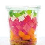A jar of layered watermelon tomato feta salad with red wine vinaigrette on the bottom.
